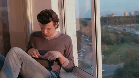 Tired man working on laptop sitting on balcony with city view at sunset in Stock Footage 102449659
