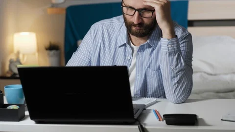 Tired man works at computer writes notes in notebook and drinking coffee or tea 動画素材 129380968