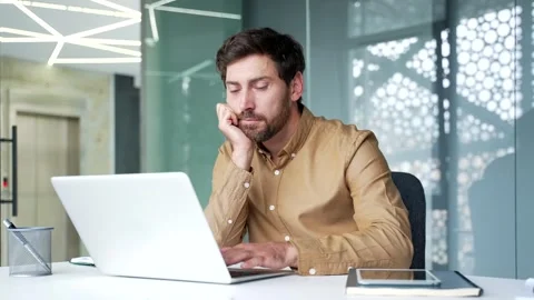 Tired mature businessman looking bored while working on a laptop at his desk  Vídeo Stock 342015341
