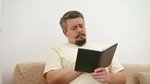 Tired middle aged man falling asleep while reading on the sofa Stock Footage 340931938