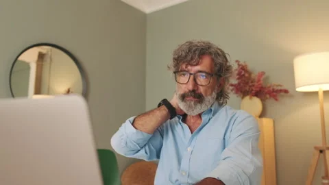 Tired middle-aged man in glasses sitting in the living room working on laptop 스톡 동영상 252207348