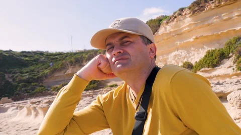 A tired middle-aged man in a yellow sweater and cap sits against a background of Stock Footage 101547840