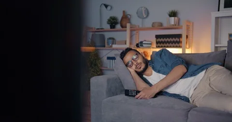 Tired Middle Eastern man sleeping on couch in front of TV lying alone Stock Footage 114492916
