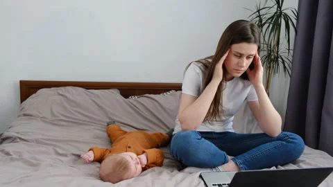 Tired mom falling asleep sitting on bed with baby daughter Stock Footage 151087306