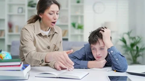 A tired mother is doing homework with her school boy child scolding her son whil Stock Footage 238632557
