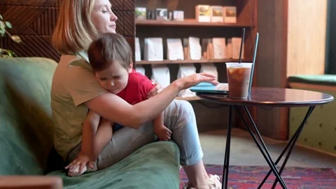 Tired mother working oh her laptop, holding her toddler son and drinking coffee Stock Footage 329599490