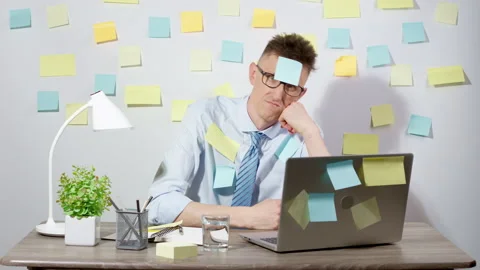 Tired office worker man sits at his desk with a laptop with pasted stickers.  Stock Footage 230507323