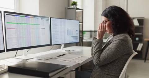Tired office worker massaging temples while analyzing data on multiple screens Stock Footage 331127175