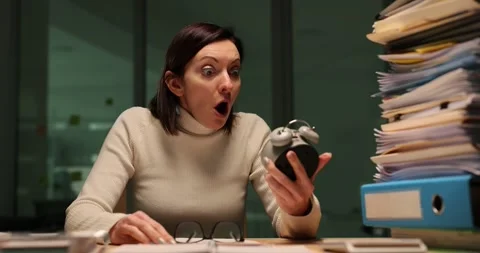 Tired office worker overloaded with work at night looks at alarm clock. Stock Footage 273690333