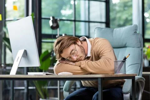 Tired programmer, IT specialist fell asleep at the workplace in the office, at Stock Photos