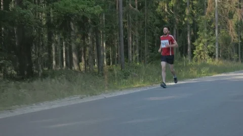 Tired runner of marathon running down the road near a forest Stockbeeldmateriaal 74551940