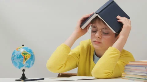 Tired school boy puts a book on his head and lying on table Video stock 172490469