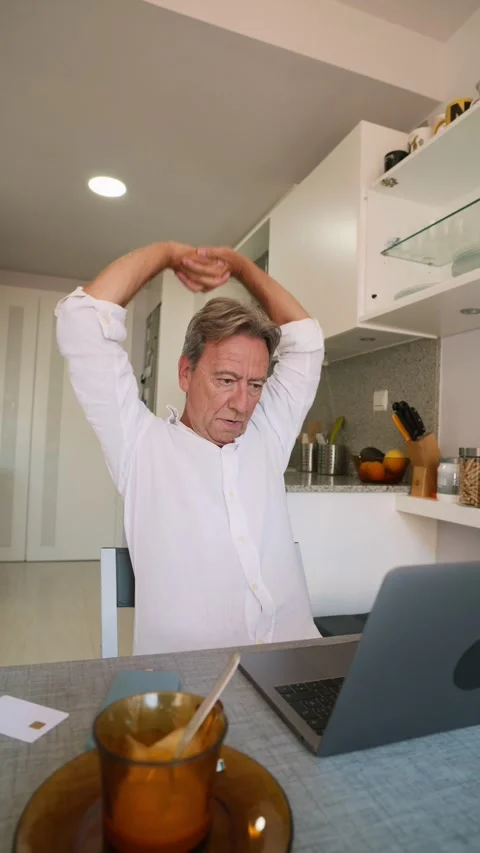 Tired senior man stretching while working remotely at home Stock Footage 343218169