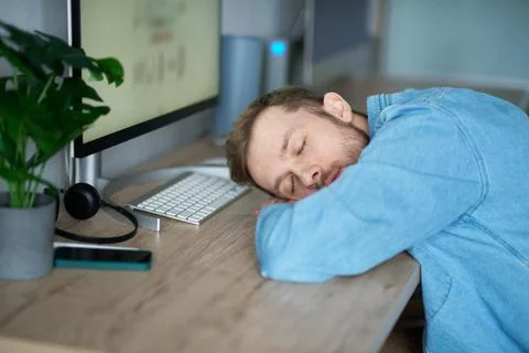 Tired software developer trying to sleep near computer at working place Stockfoto's