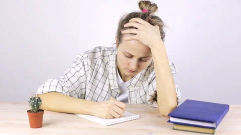 A tired student is engaged and falls asleep sitting at a table with textbooks Stock Footage 104388161