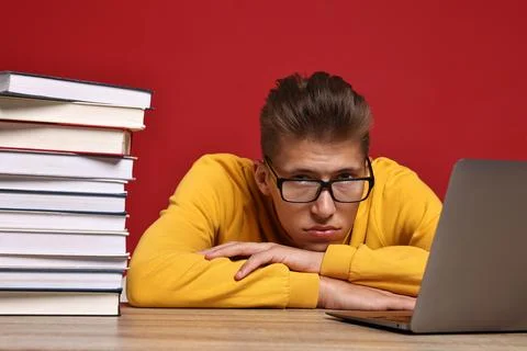 Tired student before exam with stack of books and laptop at wooden table ag.. Stock Photos