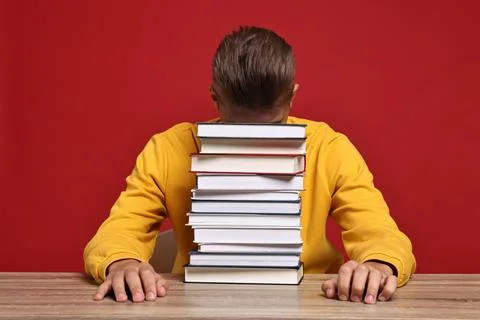Tired student before exam with stack of books at wooden table against red b.. Stock Photos