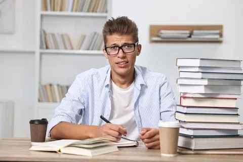 Tired student before exam with stack of books and coffee at table indoors Stock Photos