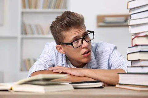 Tired student before exam with stack of books at table indoors Stock Photos