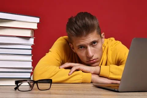 Tired student before exam with stack of books and laptop at wooden table ag.. Stock Photos