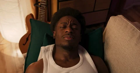 Tired student rests on the couch in the evening after a busy day, muscular 動画素材 200799033