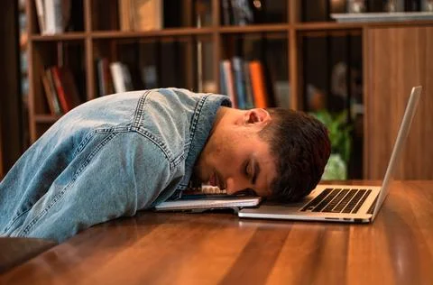 A tired student sleeping on the table inside university library. Stock Photos