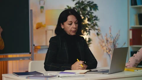 Tired teacher struggling to work while noisy pupils run around in the classroom Stock Footage 303139409