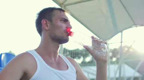 Tired of training the athlete sits on a bench and drinking water Stock Footage 56229069