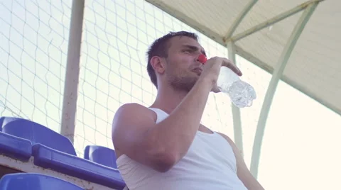 Tired of training the athlete sits on a bench and drinking water Stock Footage 56229709