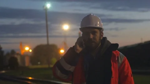 Tired worker in hard helmet talking by phone at hignt. 4k shot Video stock 83760620