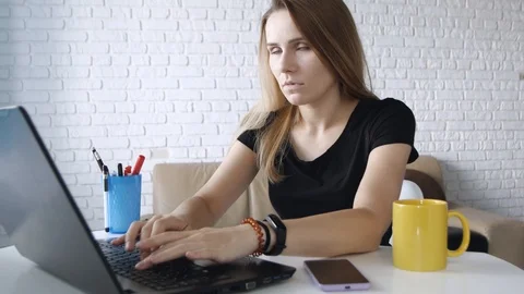 Tired working woman is using her laptop, typing while sitting at desktop over Vídeo Stock 111711148