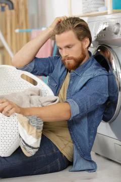 Tired young man doing laundry at home Stock Photos
