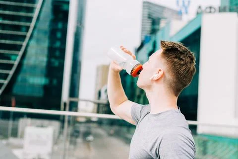 Tired Young man runner drinking water, relaxing after sport training. Holding Stock Photos