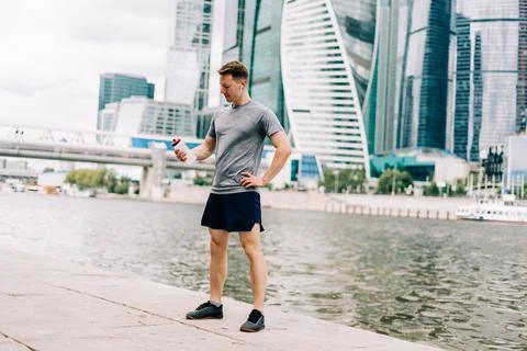 Tired Young man runner drinking water, relaxing after sport training. Holding Stock Photos