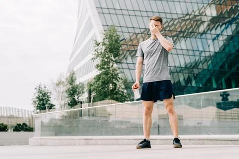 Tired Young man runner drinking water, relaxing after sport training. Holding Stock Photos