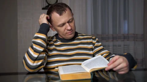 Tired young man studying the text in a book while sitting at the table Stock Footage 129060703