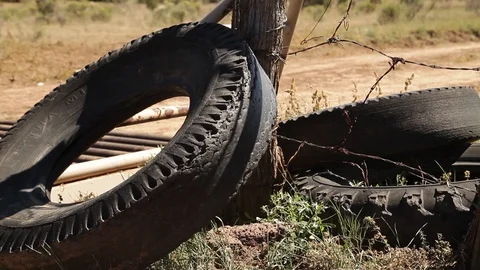 Tires lean against a post with barbed-wire on the side of a road Stock Footage 90819338
