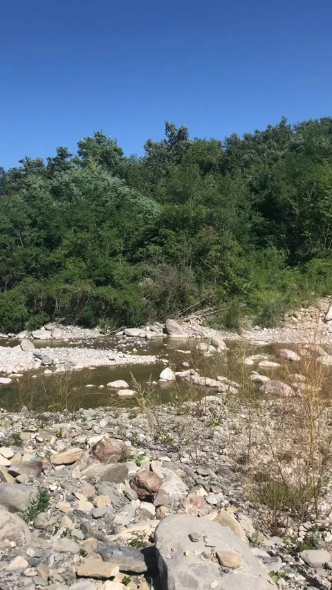 Title: A shallow rocky riverbed with low water flow winds through a mountain Stock Footage 344278511