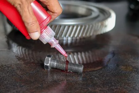 Title.Mechanic applying threadlocker fluid onto metal bolt threads using sq.. Stock Photos