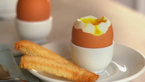 Toast bread dips in soft-boiled egg. Chicken yolk flows down egg. Breakfast Stock Footage 295258594