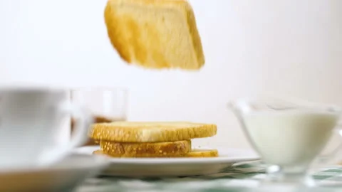 Toast bread falling down in slow motion on white plate with cup coffe and milk o 動画素材 99704486