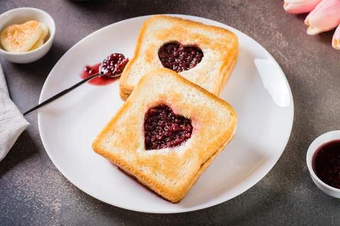 Toast with a heart filled with raspberry jam on a plate. Breakfast for a co.. Stock Photos