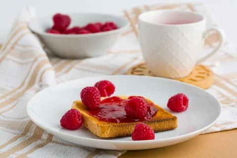 Toast with raspberry jam and cup of tea on beige table. Stock Photos