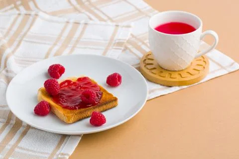 Toast with raspberry jam and cup of tea on beige table. Stock Photos