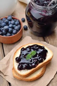 Toasted bread with blueberry jam and jam in glass jar on wooden table Stock Photos