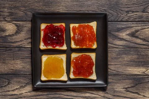 Toasted bread with different jams on square black plate on table above Fotos de archivo