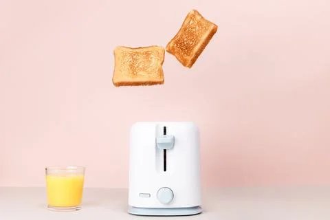 Toasted bread flew out of white toaster. Near glass of orange juice. Levitati Stock Photos