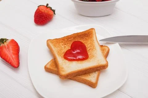 Toasted bread with jam in heart shape and strawberries on the white table. Stock Photos