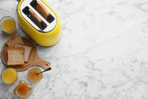Toaster with roasted bread, glasses of juice and jam on white marble table, f Stock Photos