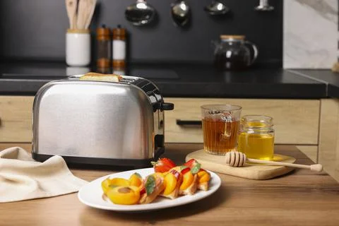 Toaster with roasted bread, tea and sandwiches on wooden table in kitchen. Ta Stock Photos